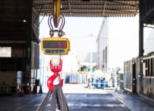 Zoomed in on a device used for weighing heavy items in a warehouse with large doors open in the background.
